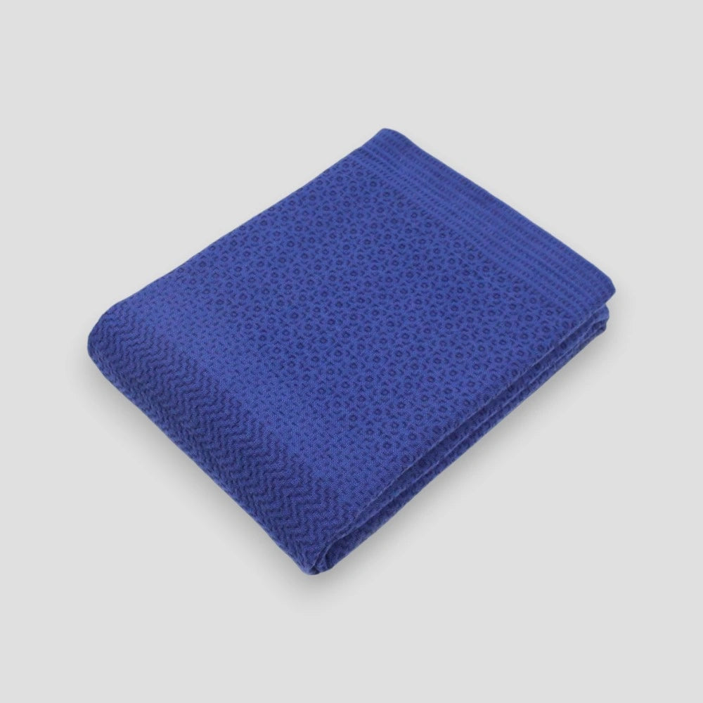 A folded blue Imabari towel with a navy geometric pattern on one side, placed on a plain background.