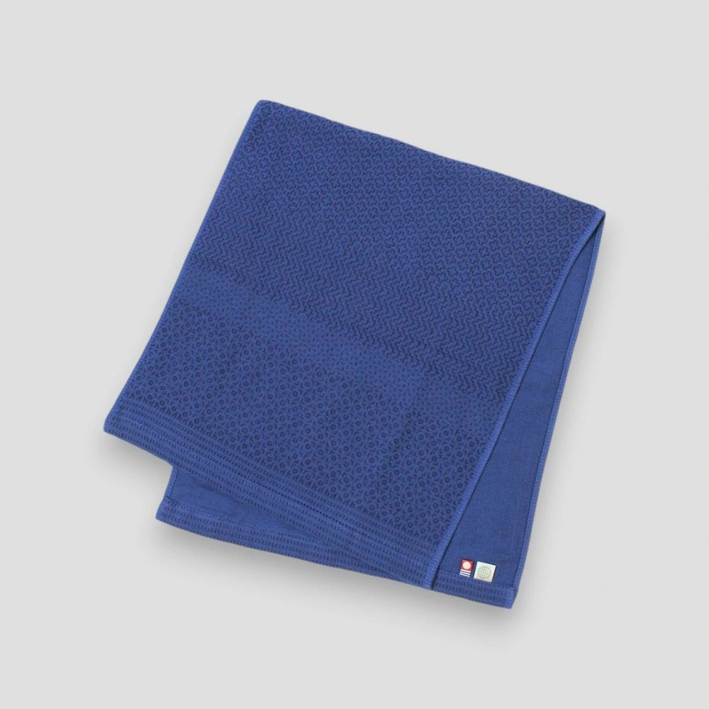 A folded blue Imabari towel with a navy geometric pattern on one side, placed on a plain background.