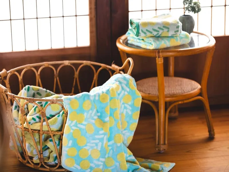 Put in the basket Imabari towels with yellow floral pattern in the blue and white fabric, two Imabari towel on the glass table