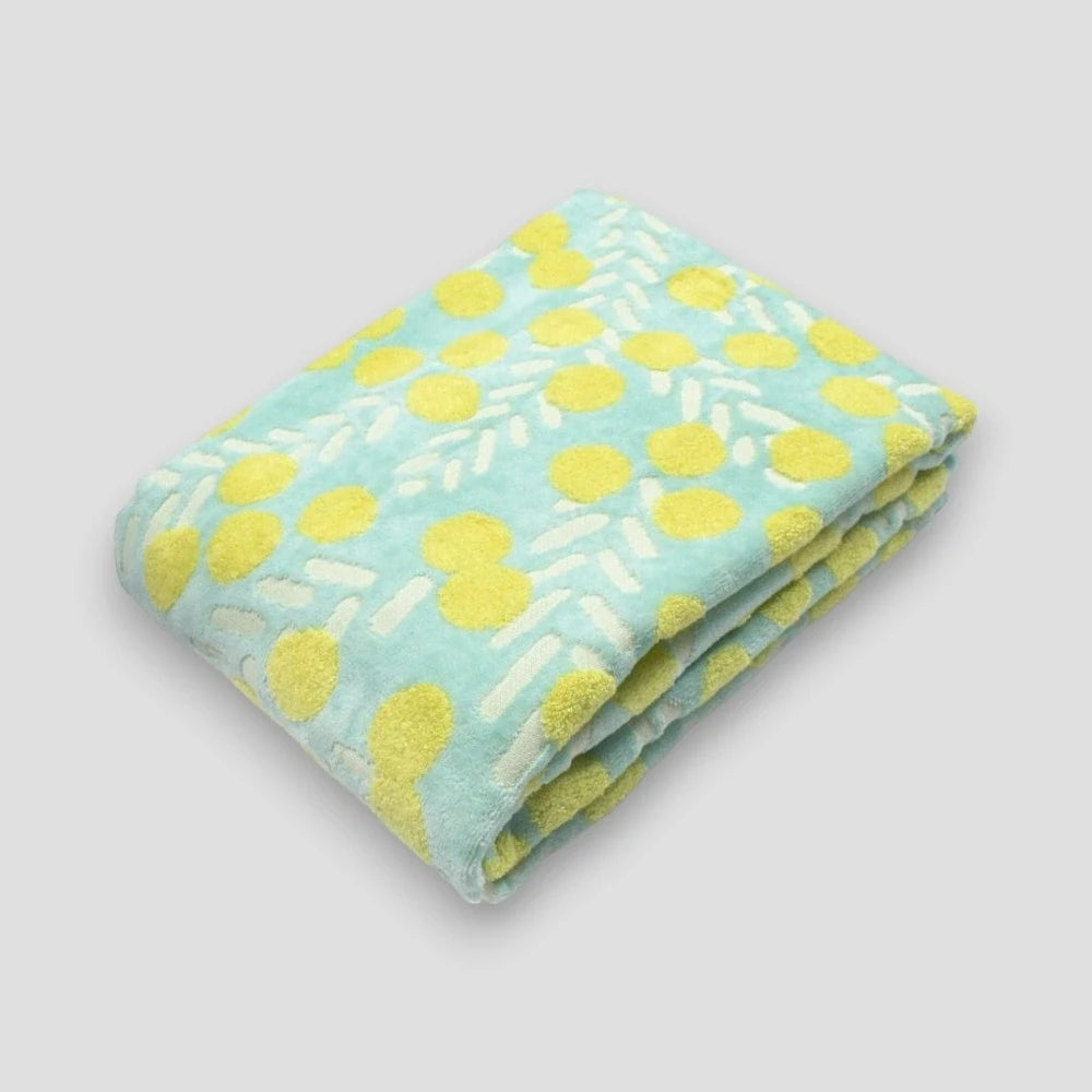 A folded cotton Imabari towel featuring a yellow floral pattern with white and blue fabric on a light gray background.