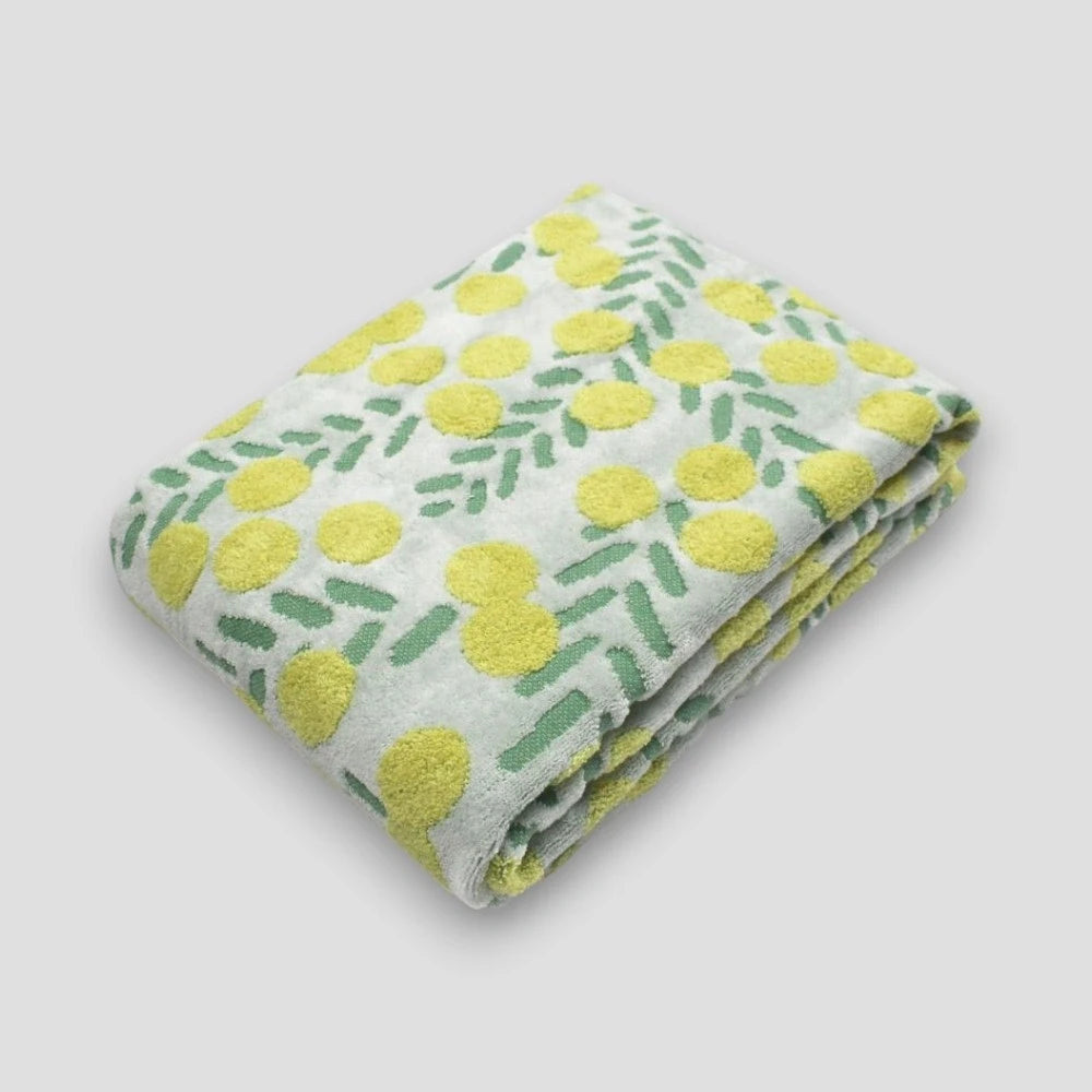 A folded cotton Imabari towel featuring a yellow floral pattern with white and green fabric on a light gray background.