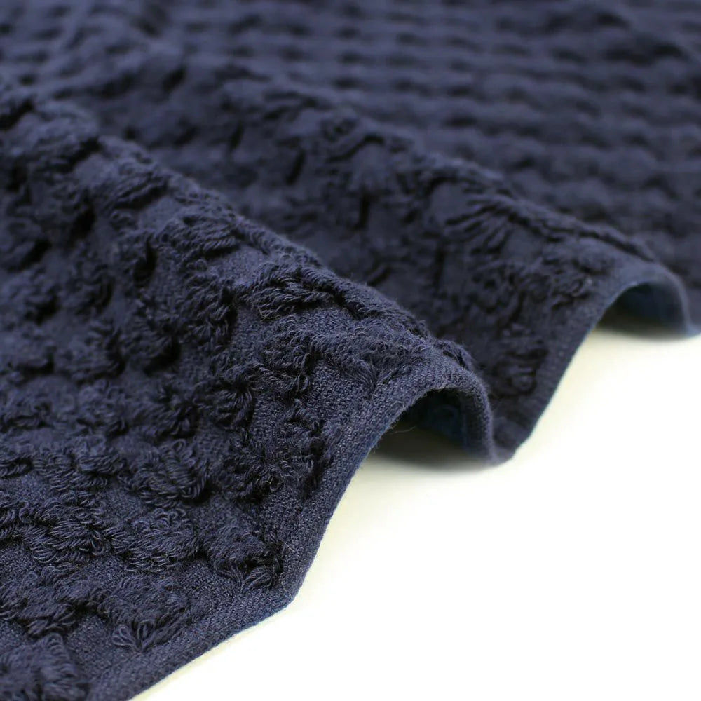 Close-up navy jacquard weave Imabari towel corner with a textured design on a light gray background.