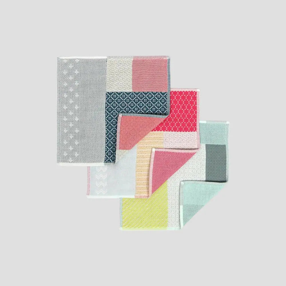 A collection of colorful patchwork design Imabari towels in various colors including yellow, red, pink, navy blue, and light gray, displayed in an overlapping arrangement.