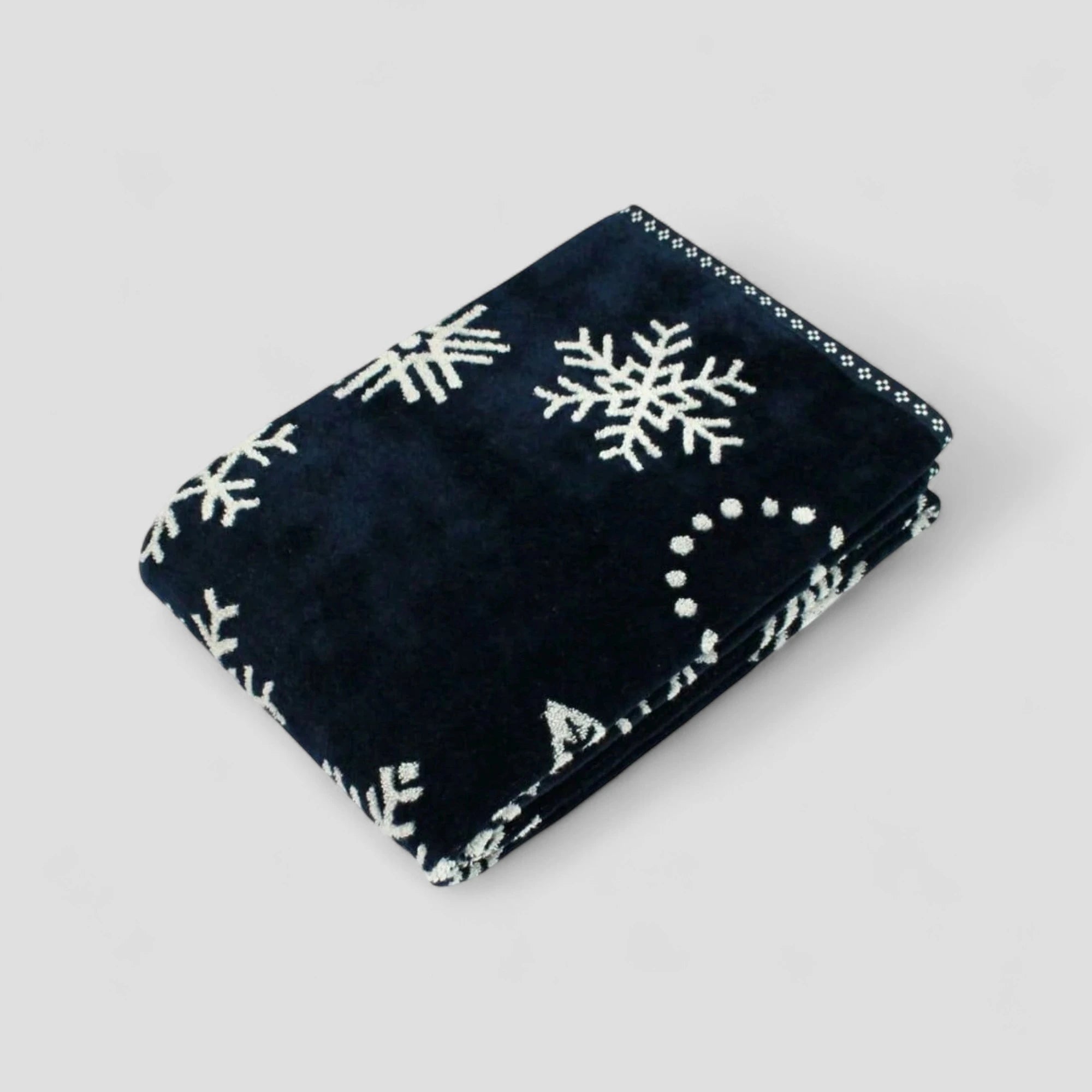 Folded navy Imabari towel with white snowflake patterns on a light gray background