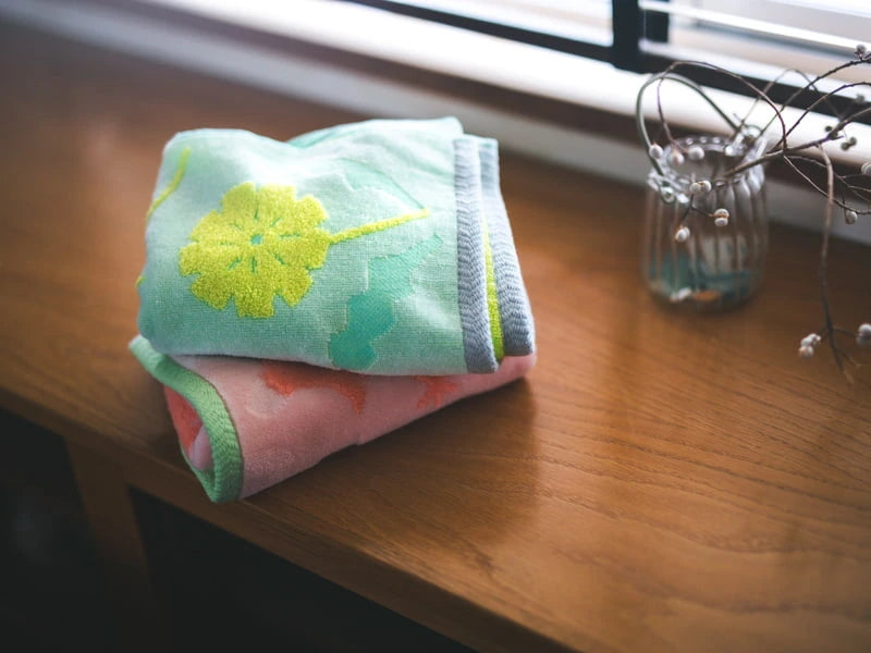 Close up of small Imabari towels in pink and green with floral patterns, made from cotton, on a white background.