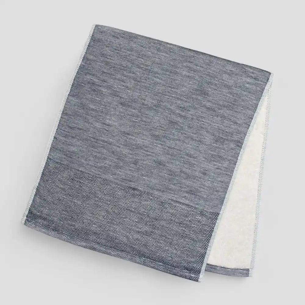 Folded navy Imabari towel with a subtle herringbone pattern on a light gray background.