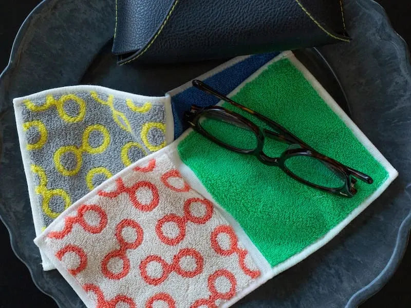 Two compact Imabari towels in vibrant patterns leave on the plate beside a glasses