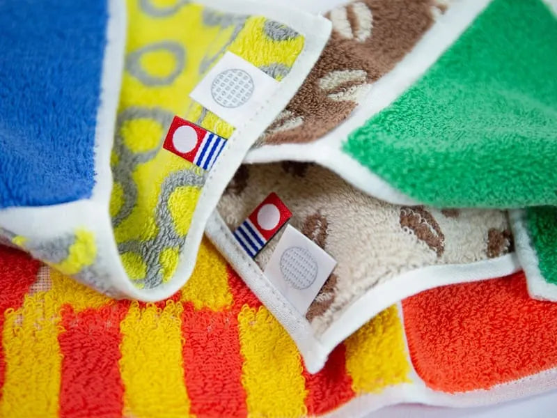 Close up of vorious compact Imabari towels in vibrant patterns with labels of Imabari towel brand mark and Iori&