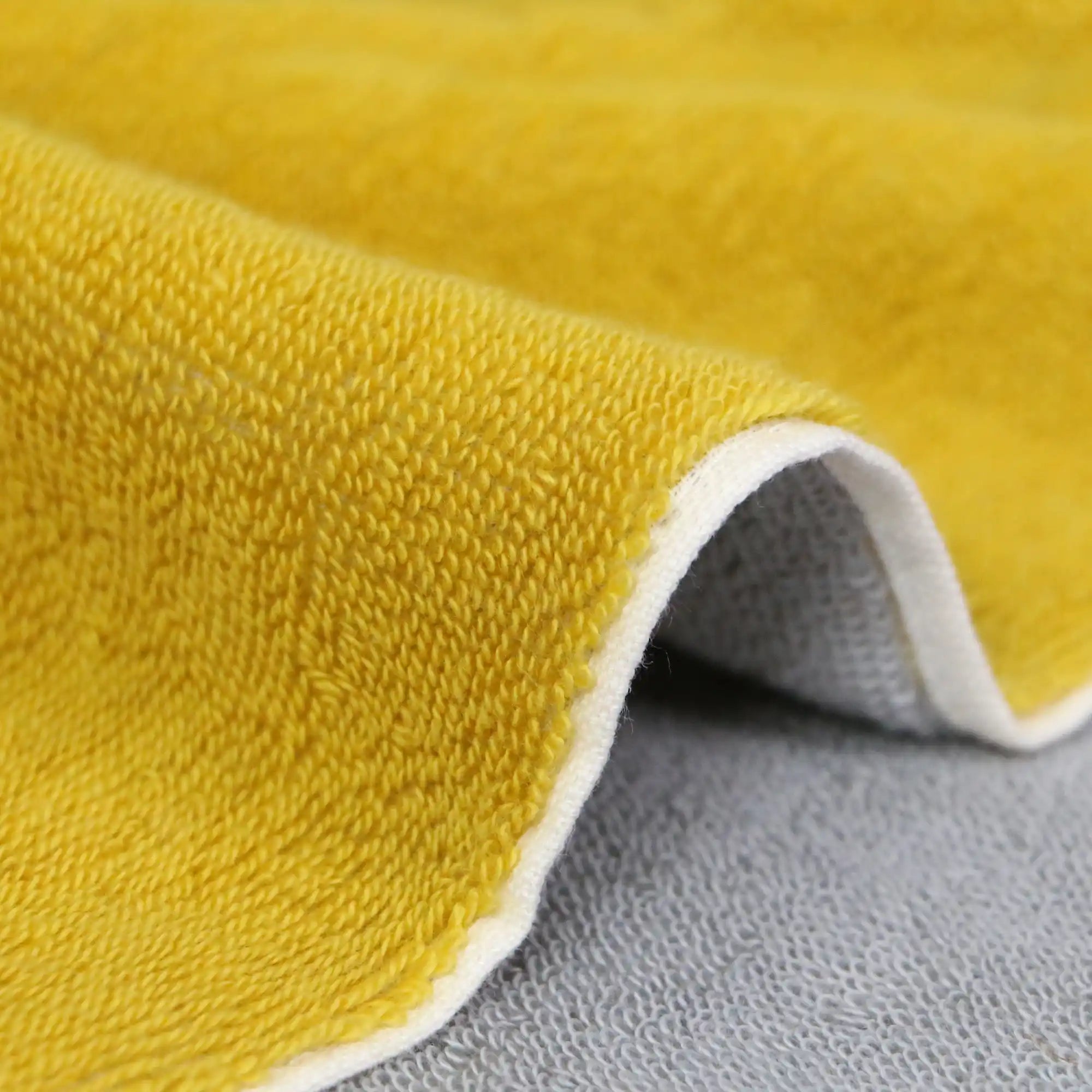 A close-up of the texture and side of a reversible yellow and gray Imabari towel