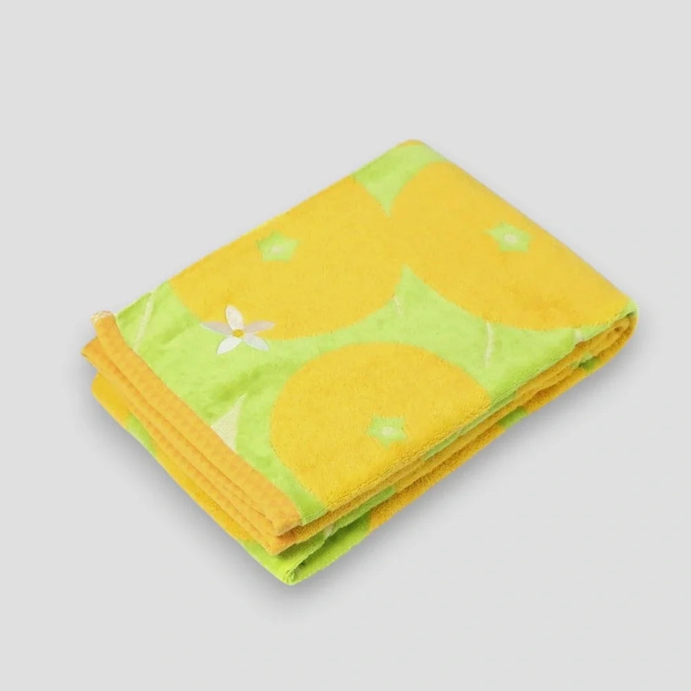 Folded yellow Imabari towel featuring a pattern with the Iyokan citrus fruit and green leaves on a white background
