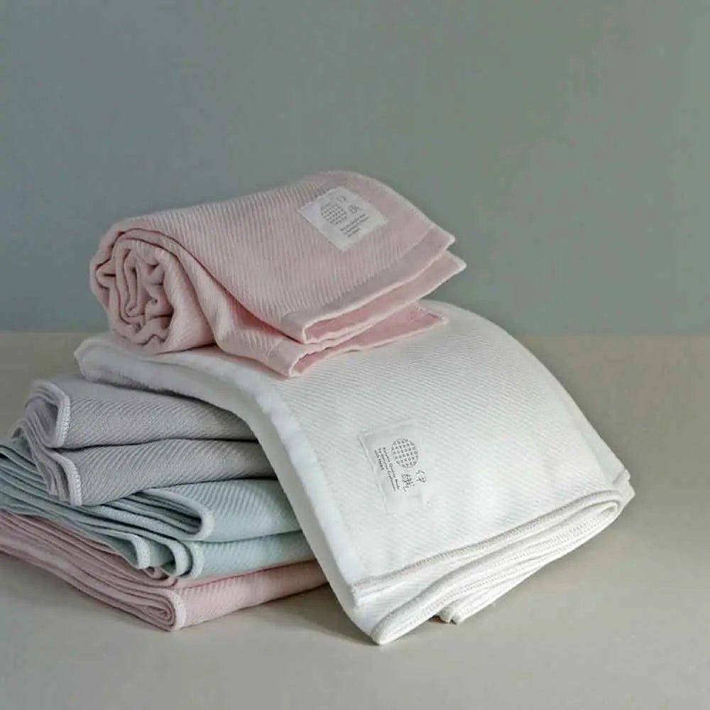 Stack of folded Imabari towels in white, pink, and blue colors made from cotton gauze, branded with a label showing the name &
