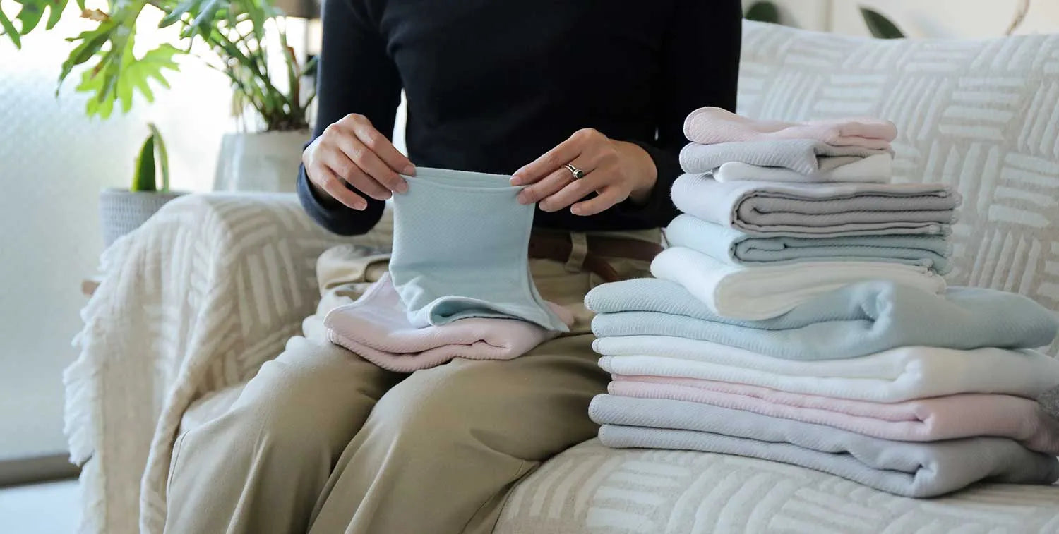 Stack of folded Imabari towels in white, pink, gray and blue colors made from cotton gauze, someone is folding Imabari towels.