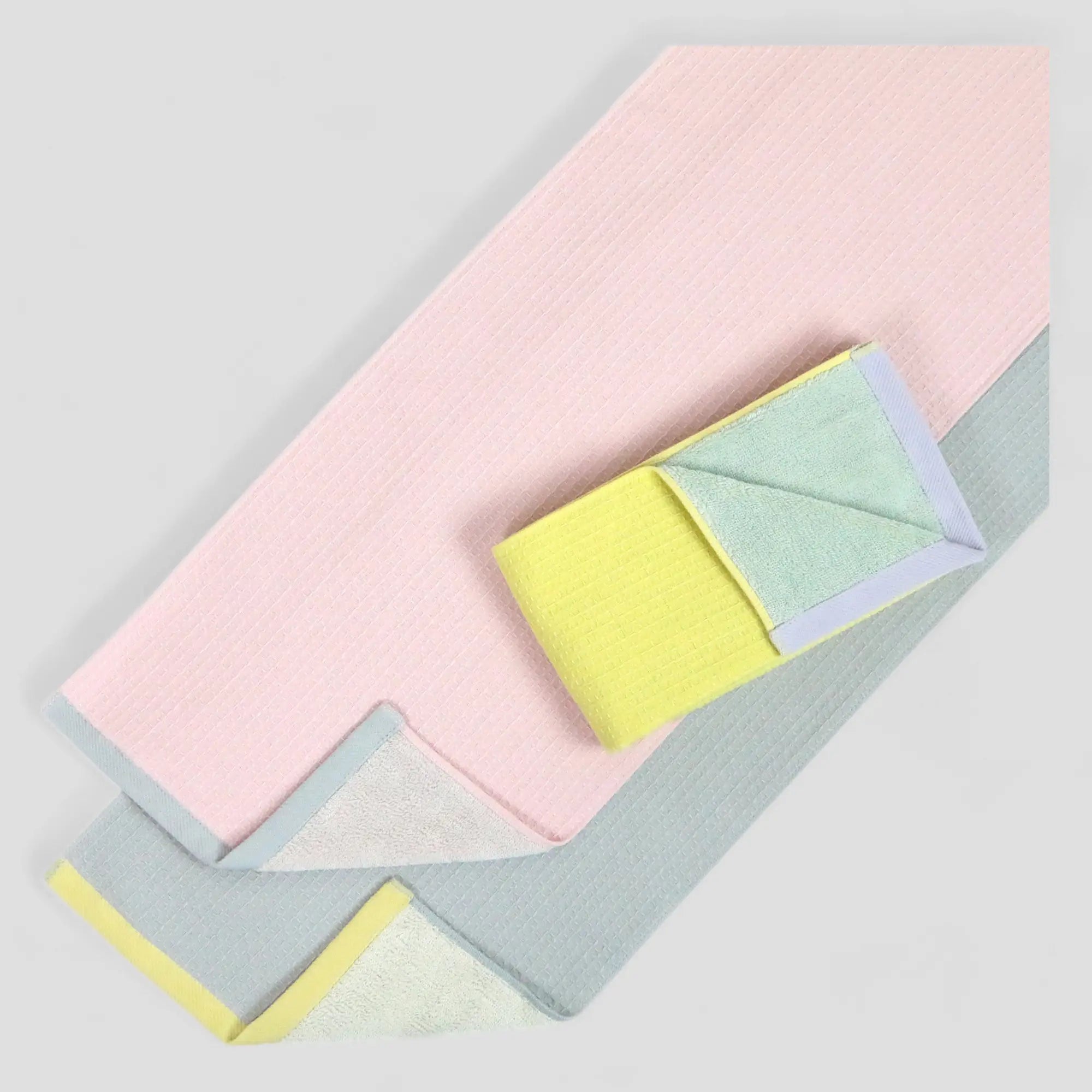 A collection of sports Imabari towels in pink, yellow, blue, and gray, featuring a waffle weave texture on one side and a cotton material on the other.