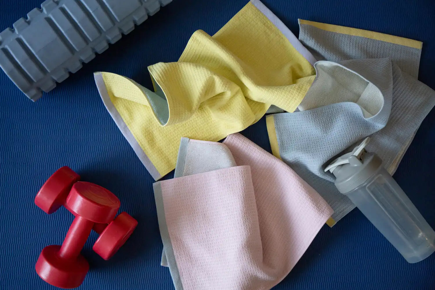 Three colors of Imabari sports towels and exercise equipment on a blue mat