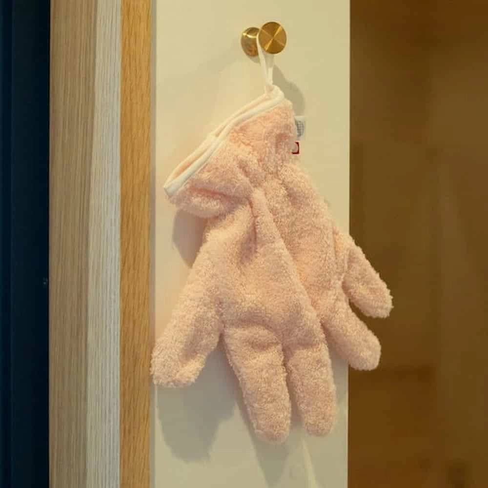Pink Imabari towel hair-dry-glove hanging on a gold hook against a white wall.