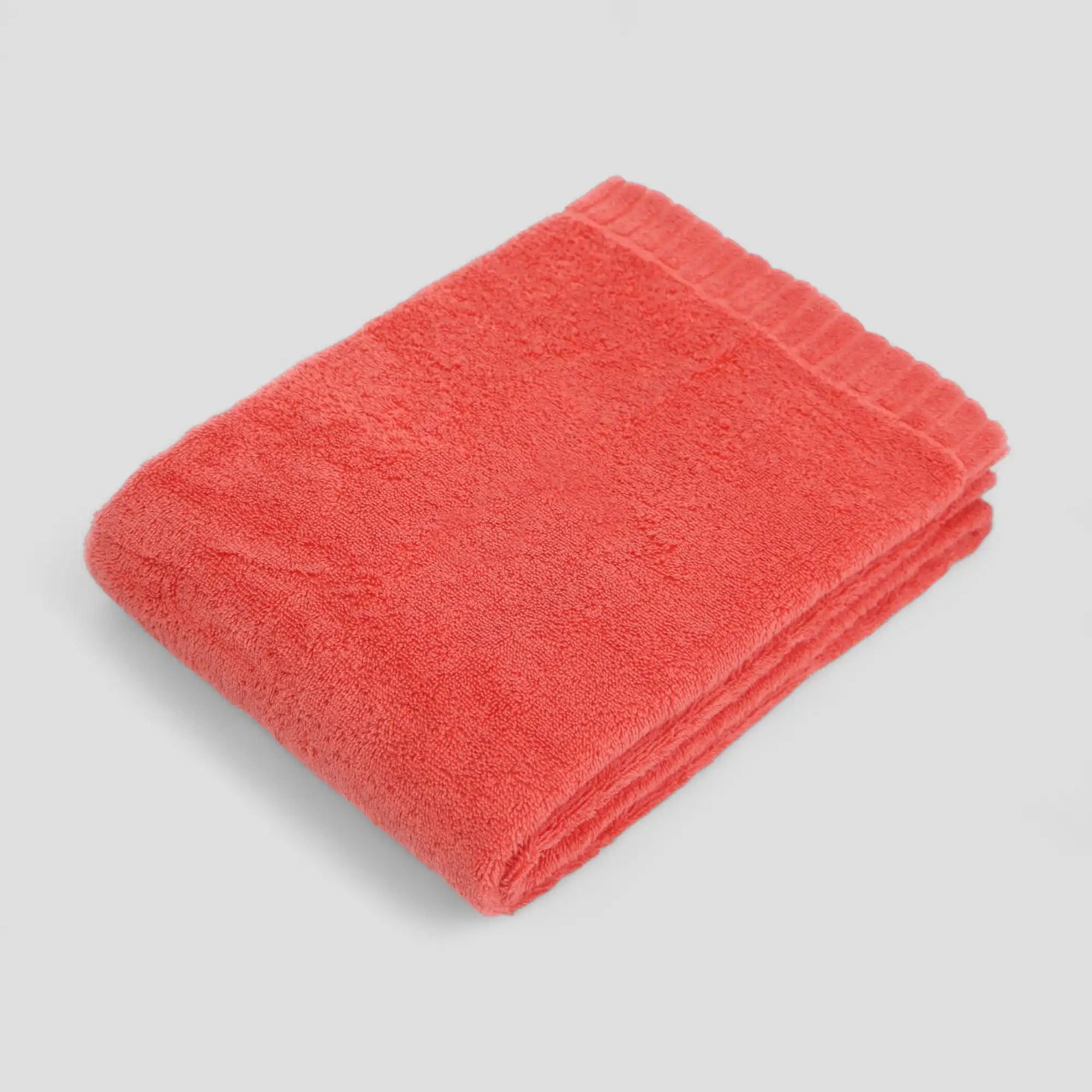 Folded coral-colored Imabari towel on a light gray background