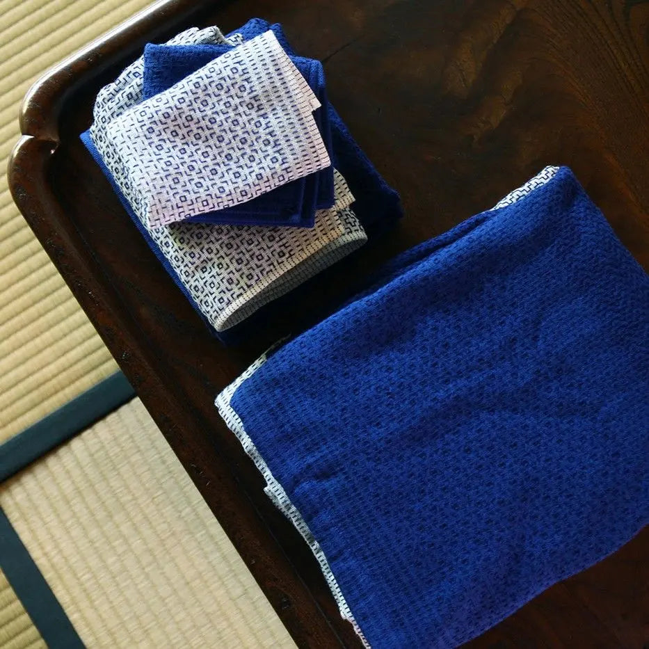 Folded blue and white Imabari towels with a geometric pattern on a wooden table.