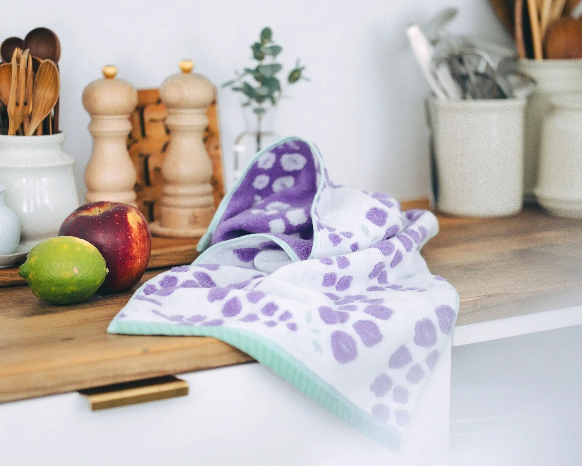 Purple and white patterned Imabari towel on a kitchen counter with utensils and fruits in the background