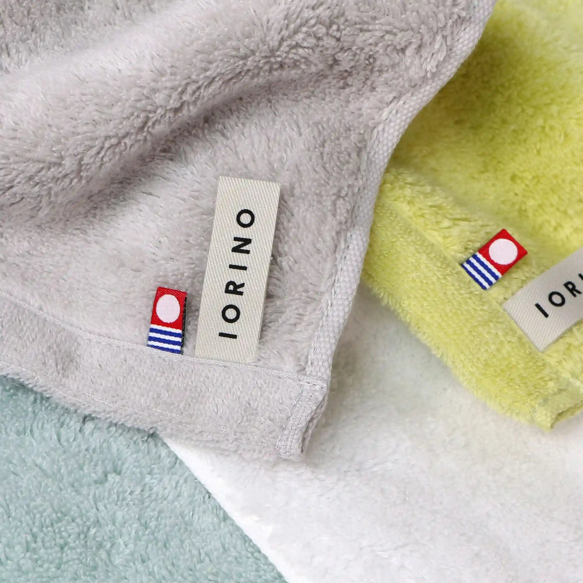 Close-up of IORINO Imabari towel branded fabric tags on various colored fabrics.