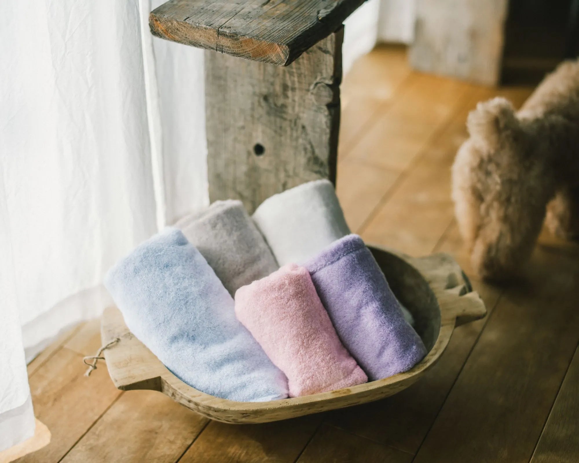 Set of colorful Imabari towels in a wooden basket on a wooden floor.