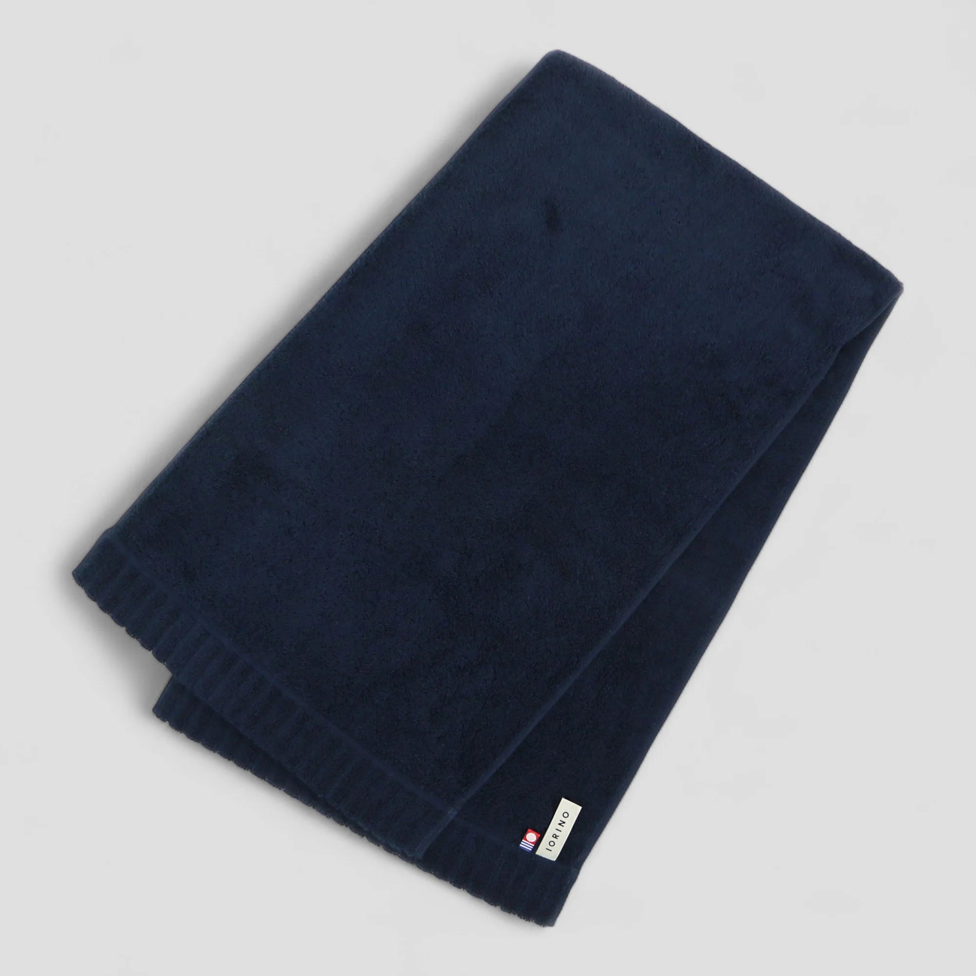 Folded navy blue Imabari towel with a brand label on a light gray background