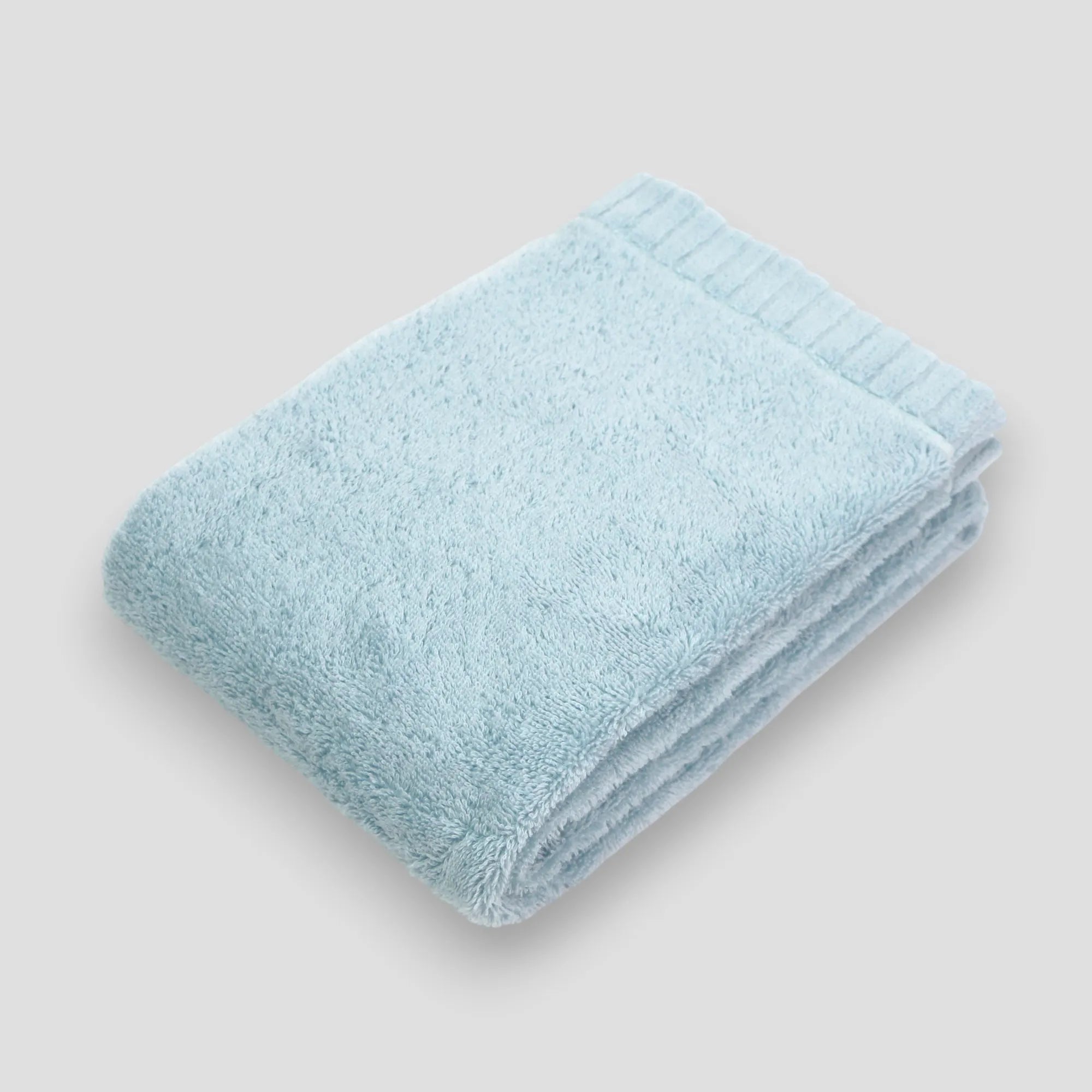 Folded light blue Imabari towel on a gray background