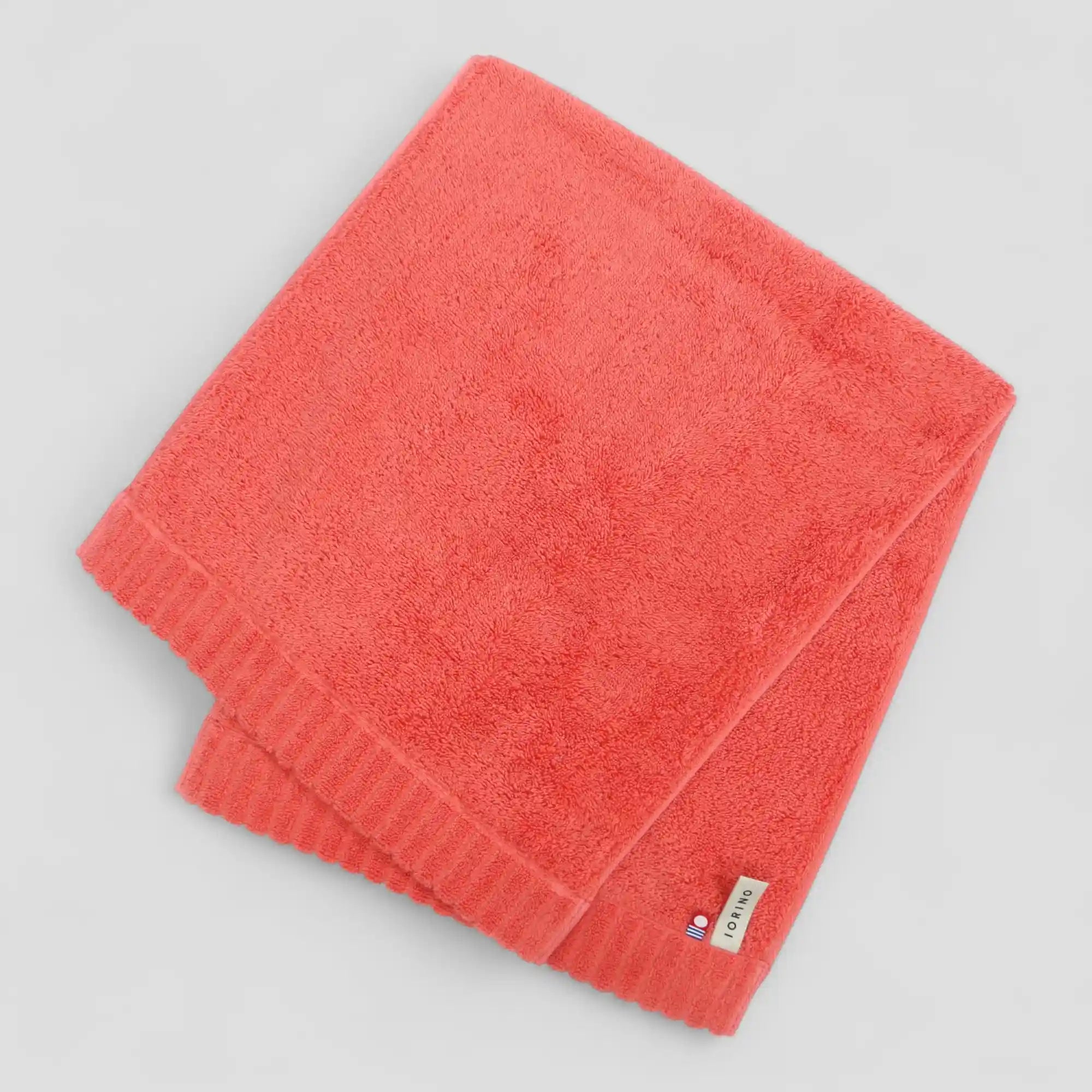Folded coral-colored Imabari towel with a brand label on a light gray background
