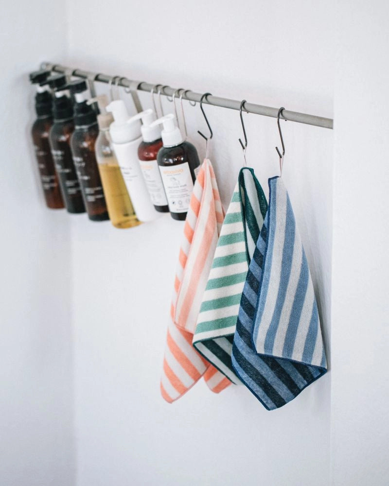 Colorful striped Imabari towels hanging on a rack with skincare products in the background.
