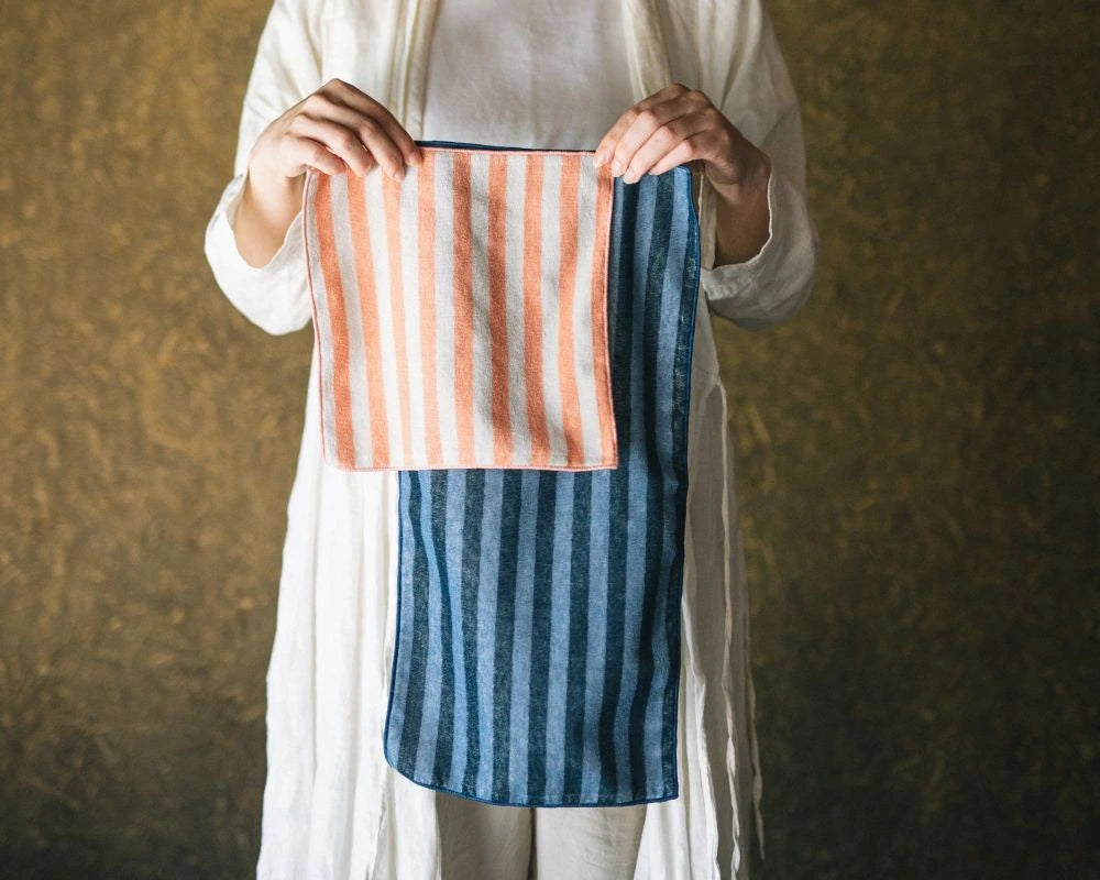 Person holding a striped Imabari towel with pink and blue patterns against a textured brown background