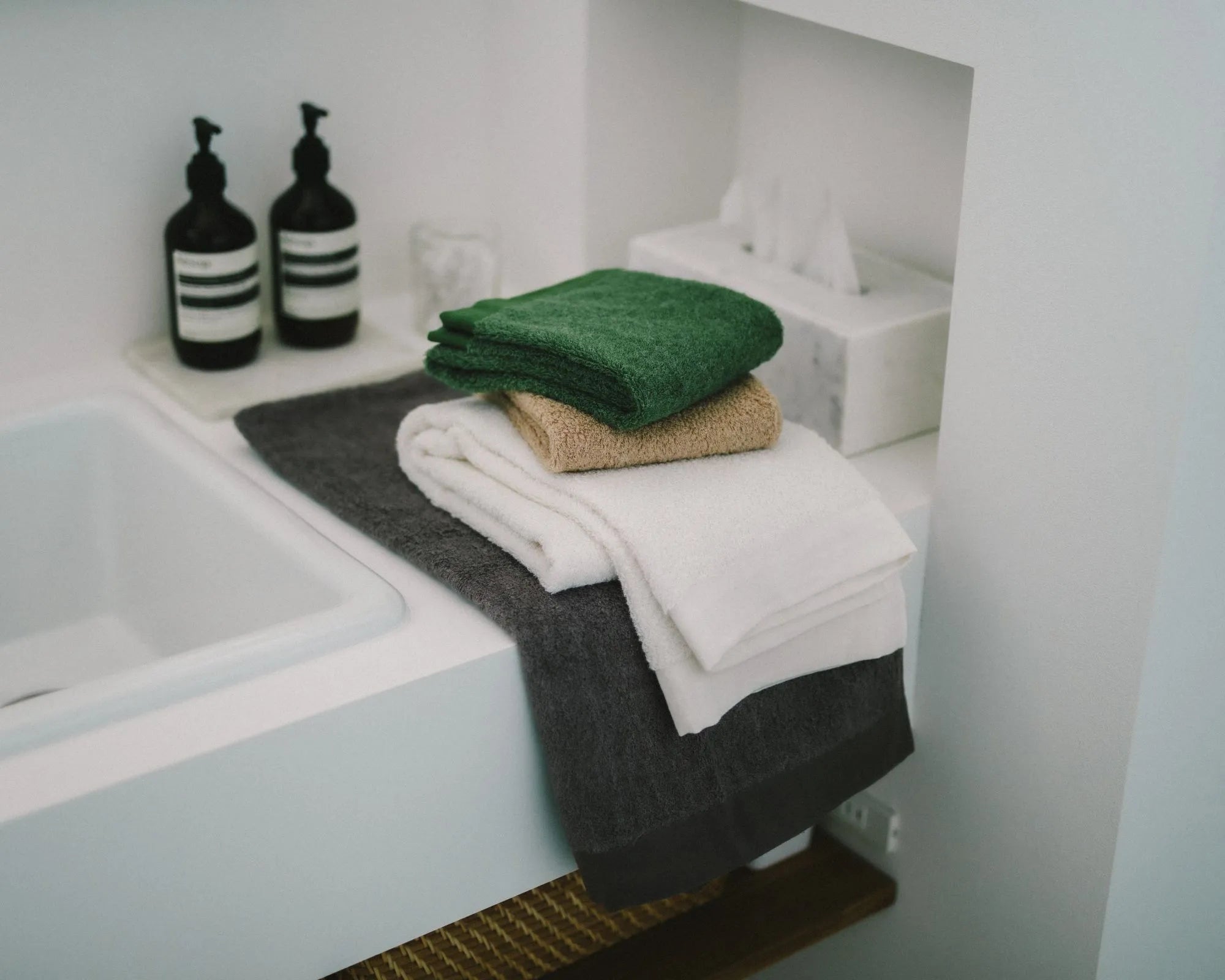 Imabari towels stacked on a sink with bottles in a bathroom setting