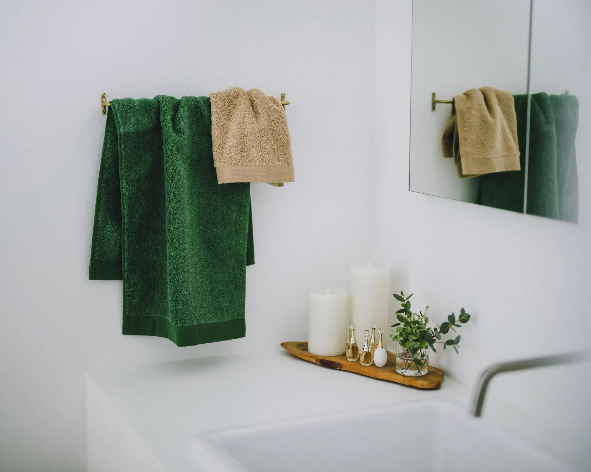 Bathroom with green and beige Imabari Towels hanging on a rack, candles, and a plant on a white countertop.