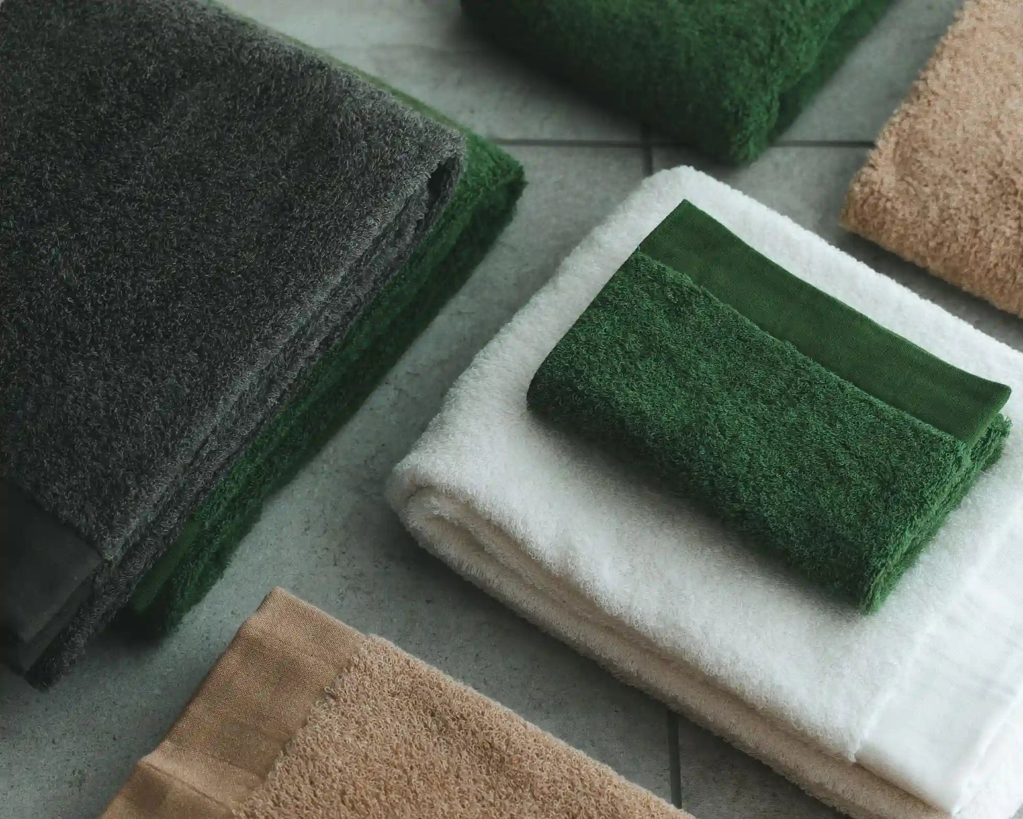 Set of folded Imabari Towels in various colors on a concrete surface.