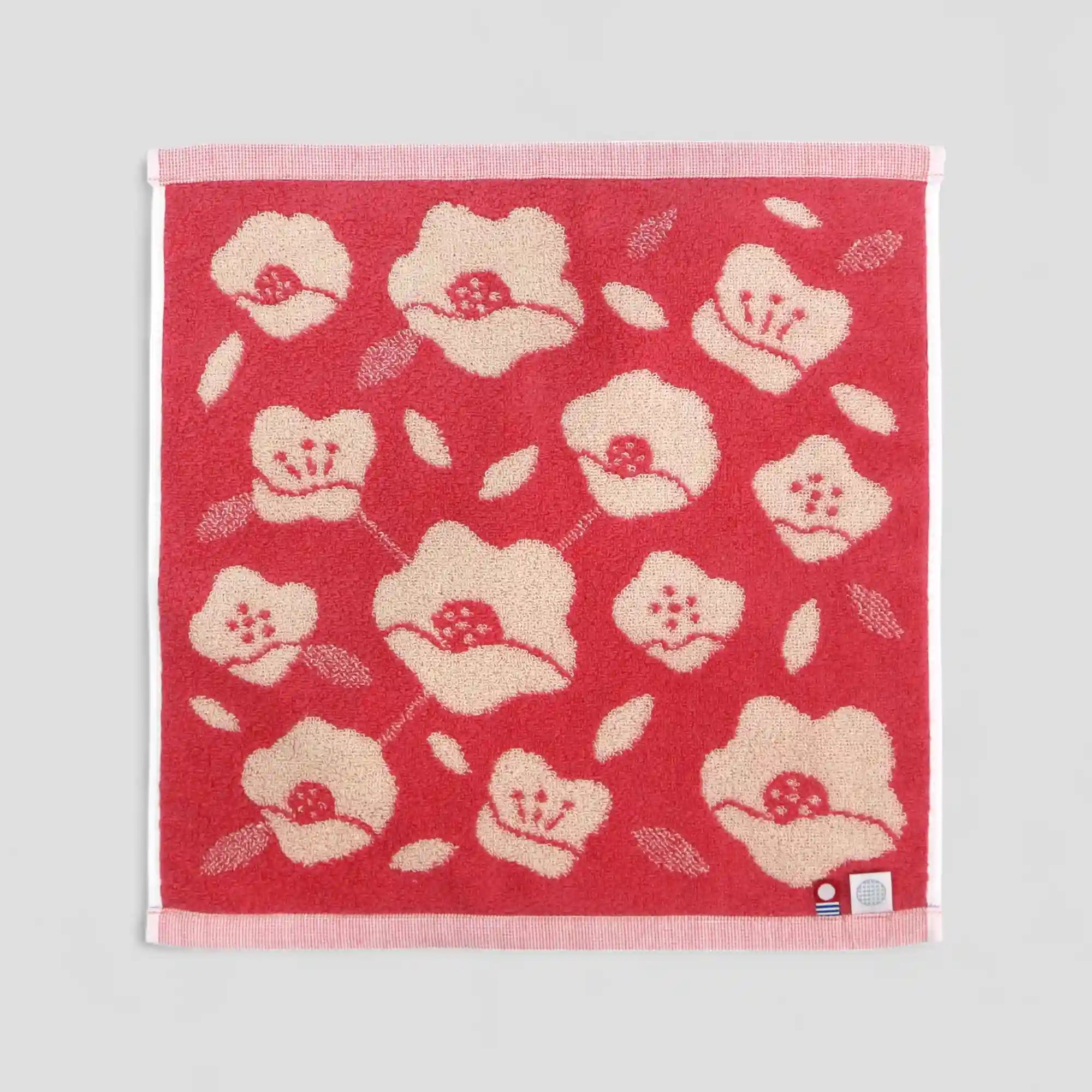 Beige floral patterned red Imabari towel with showing labels of Imabari towel brand mark and IORI&