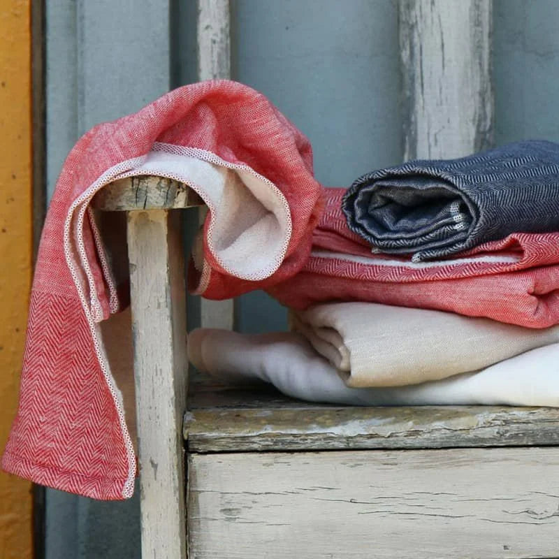 Stack of folded Imabari towel in red, white, and blue on a wooden chair.