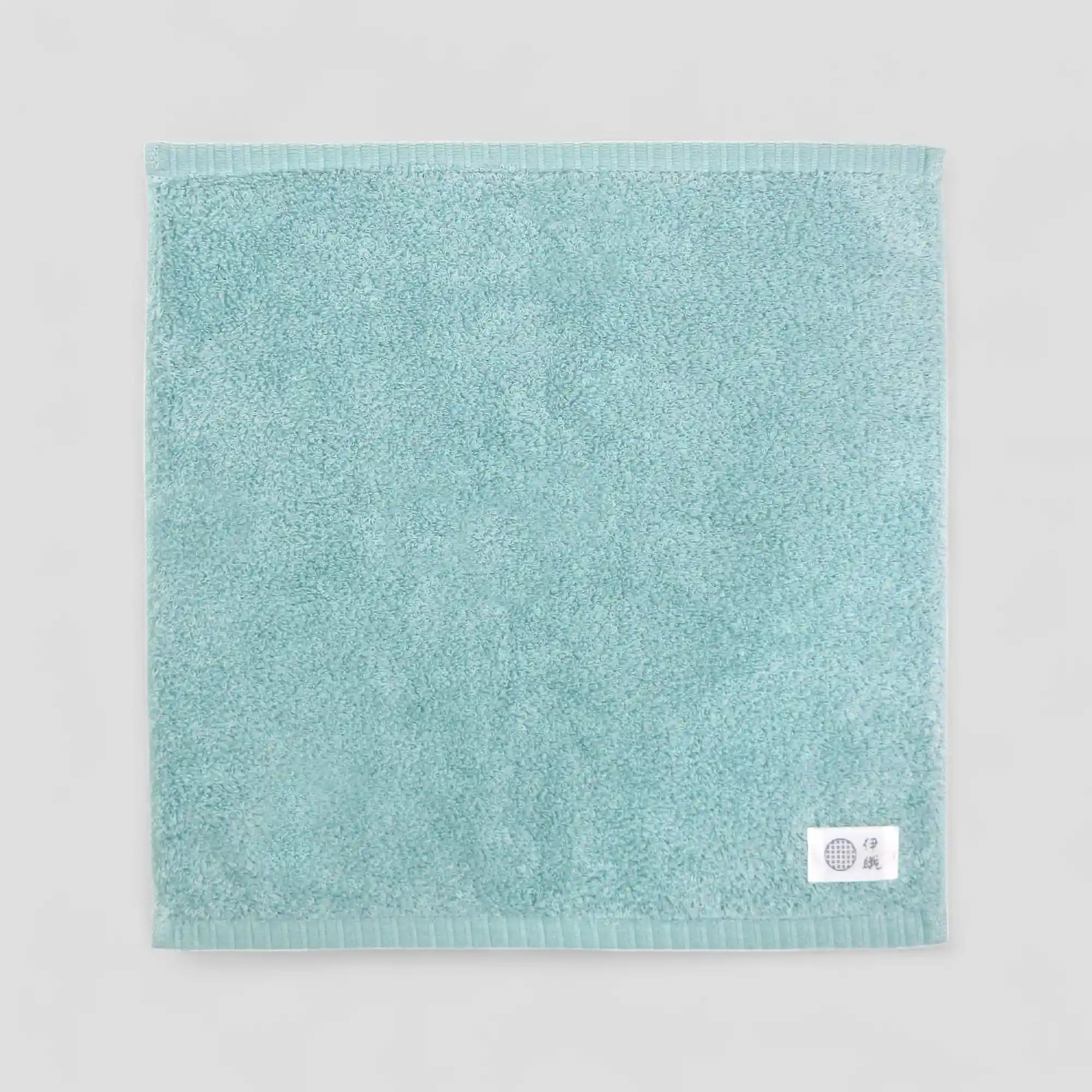 Mint-blue Imabari towel with a brand label on a light gray background