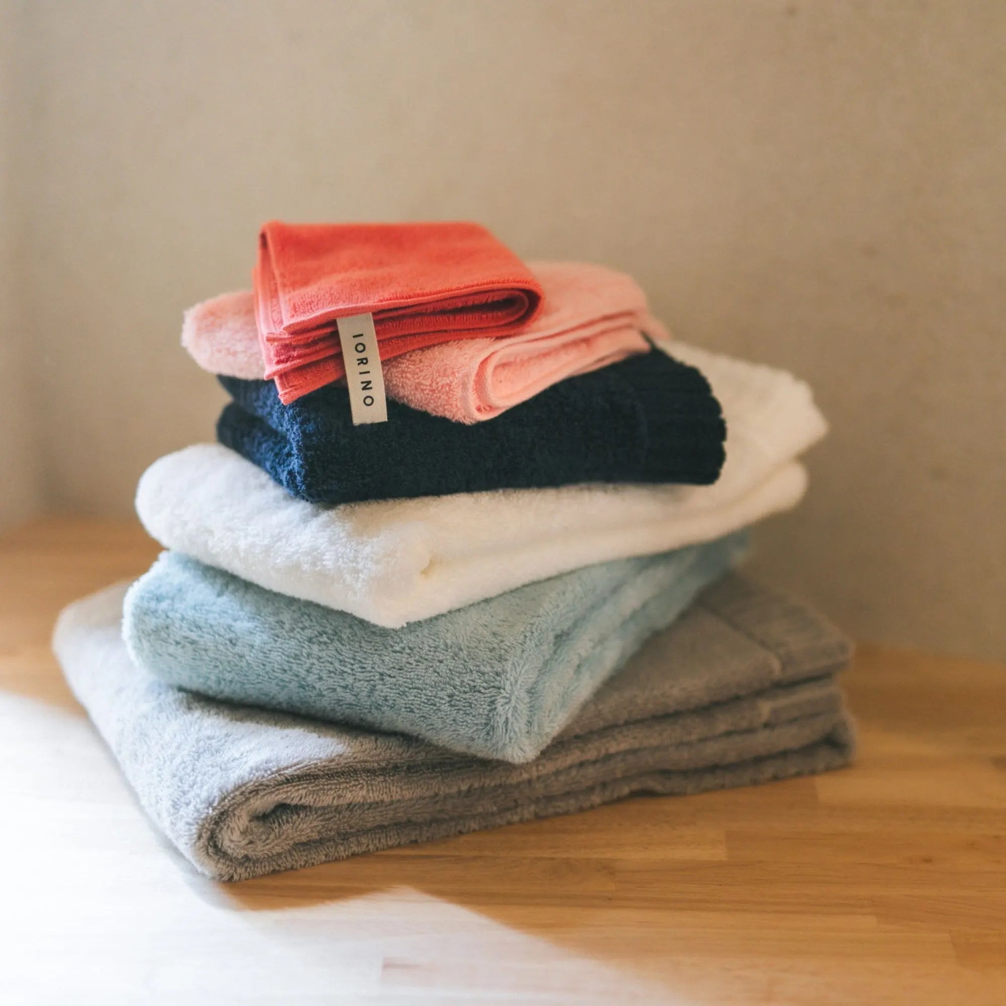 Stack of folded Imabari towels in various colors on a wooden surface.