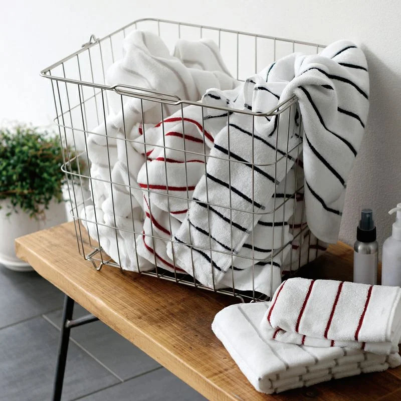 White Imabari  towels with red, gray and navy  stripes in the basket and folded white Imabari towels with red and gray stripes on wooden table 