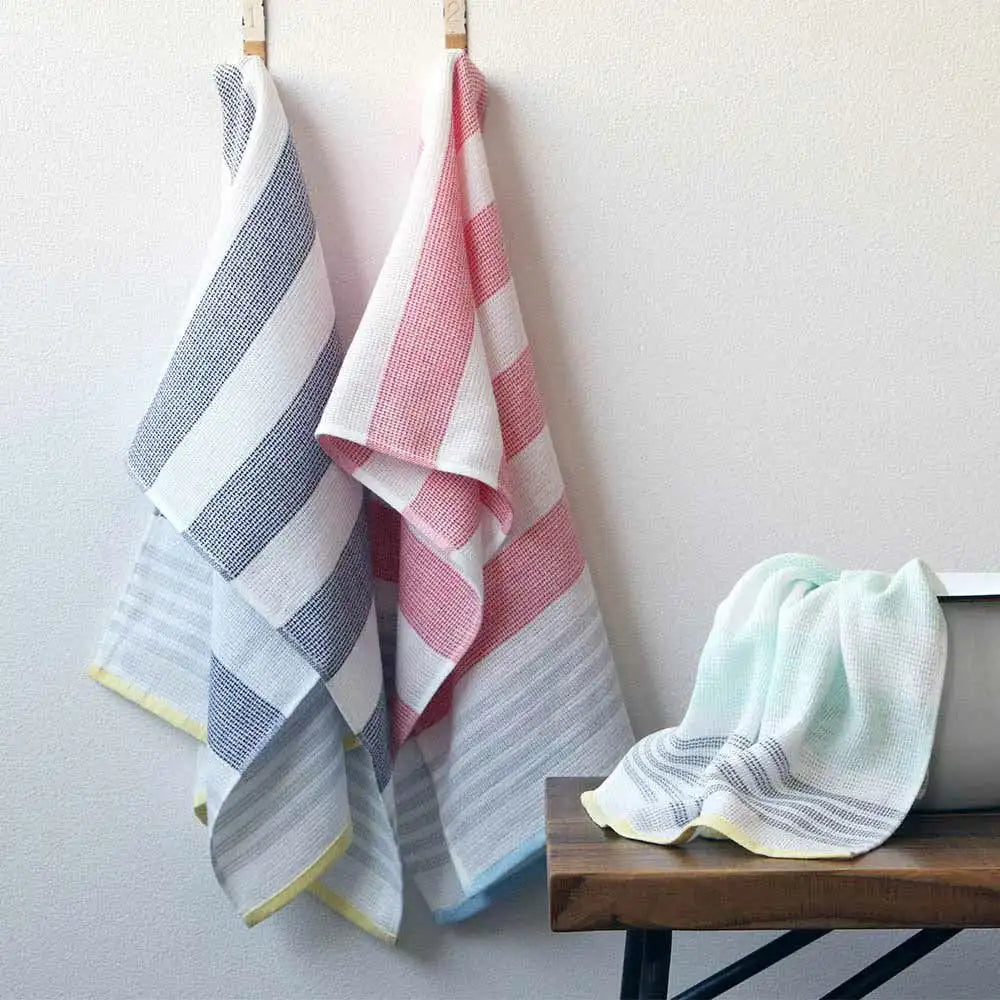 A set of colorful striped Imabari towel  wash cloths hanging on a rod against a light background, with one wash cloth laid out on a surface showing a soft, textured weave.