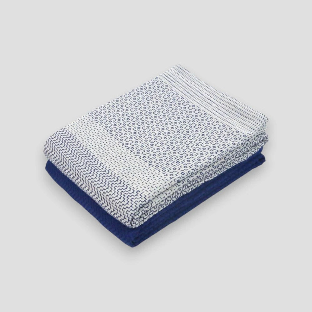A folded white and blue Imabari towel with a geometric pattern on one side on  a light gray background.