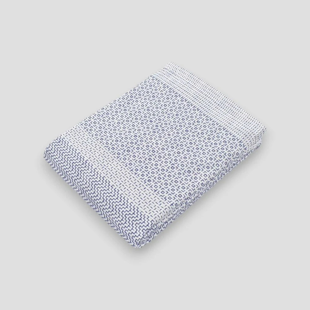 A folded white Imabari towel with a blue geometric pattern on one side, placed on a plain background.