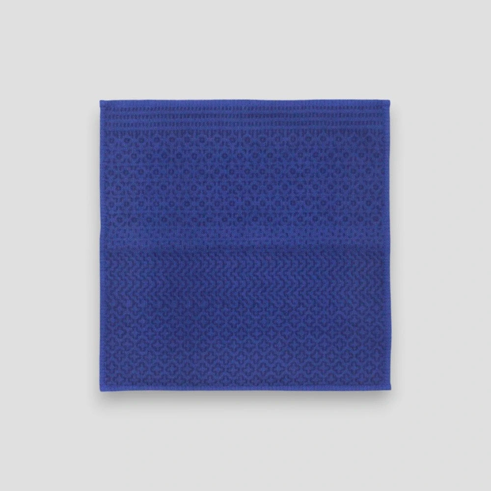 A blue Imabari towel with a navy geometric pattern on one side, placed on a plain background.
