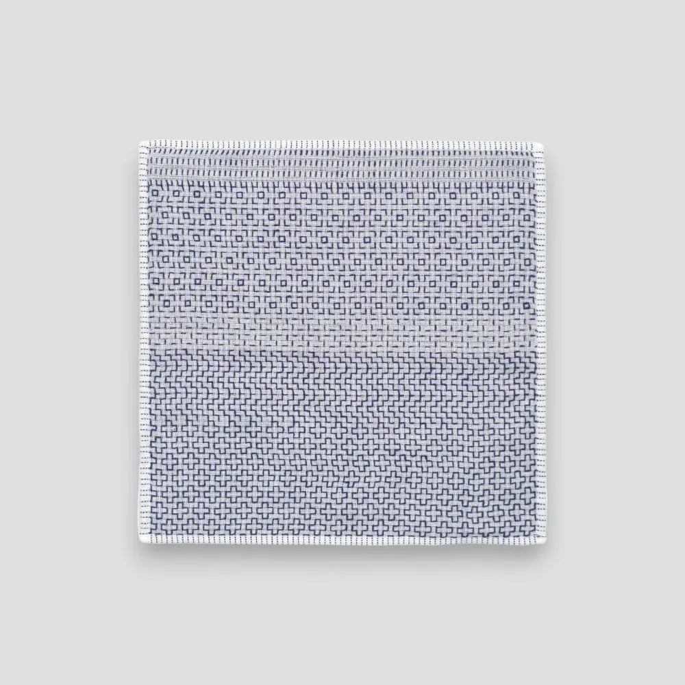A white Imabari towel with a blue geometric pattern on one side, placed on a plain background.