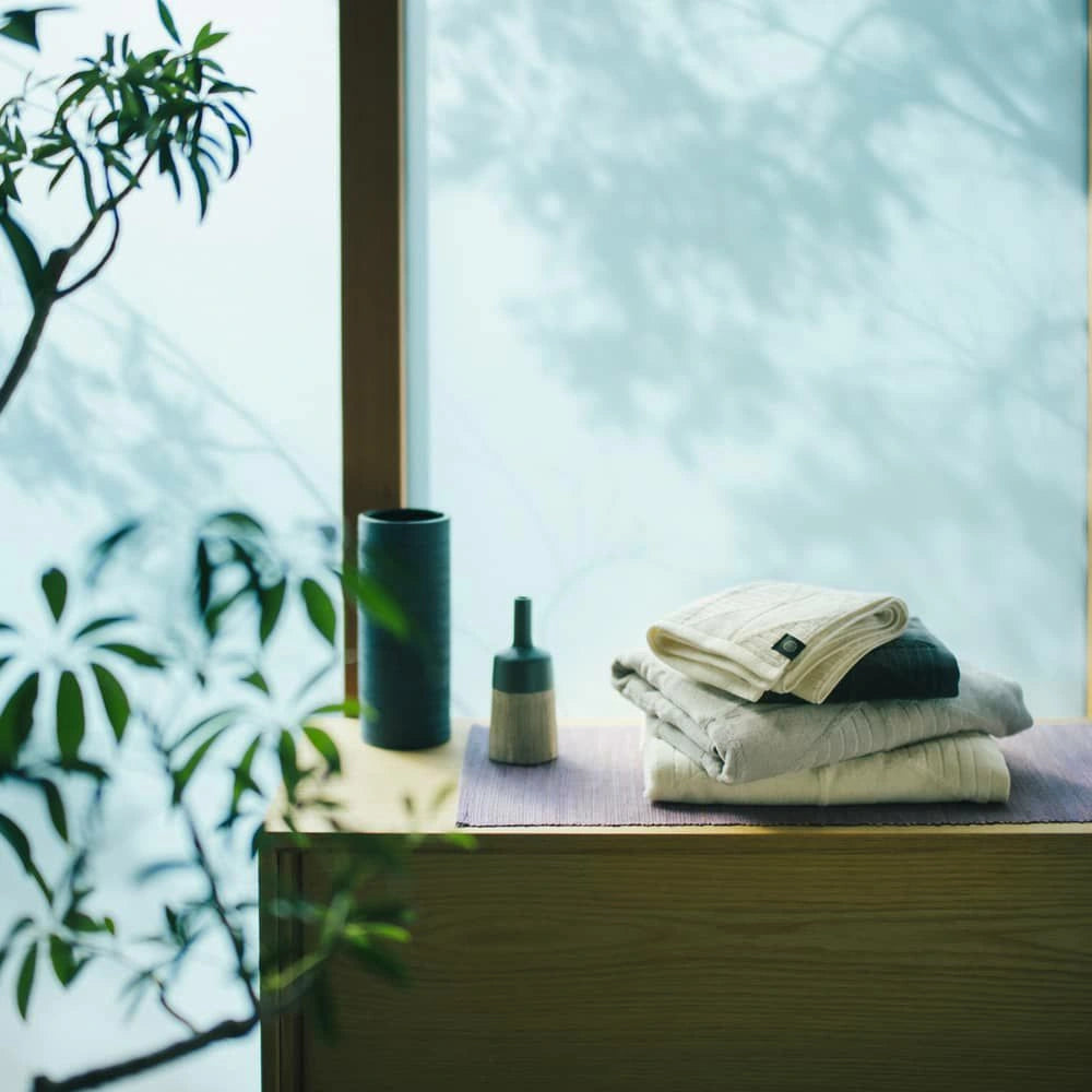 Stack of folded Imabari towels in various colors on a wooden surface.