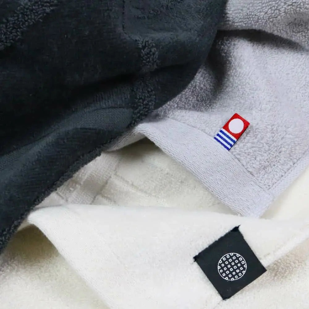 Close-up of charcoal, white, and gray Imabari towels with labels.