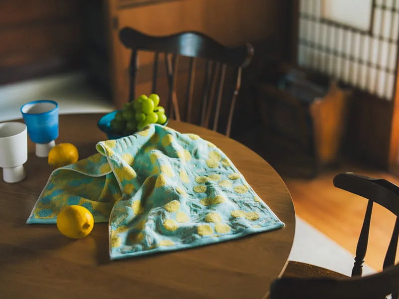 A blue Imabari towel with yellow floral pattern leave on the wooden table