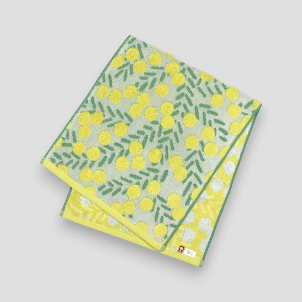 A white Imabari towel with yellow floral pattern showing tha labels of Imabari towel brand mark and IORI&