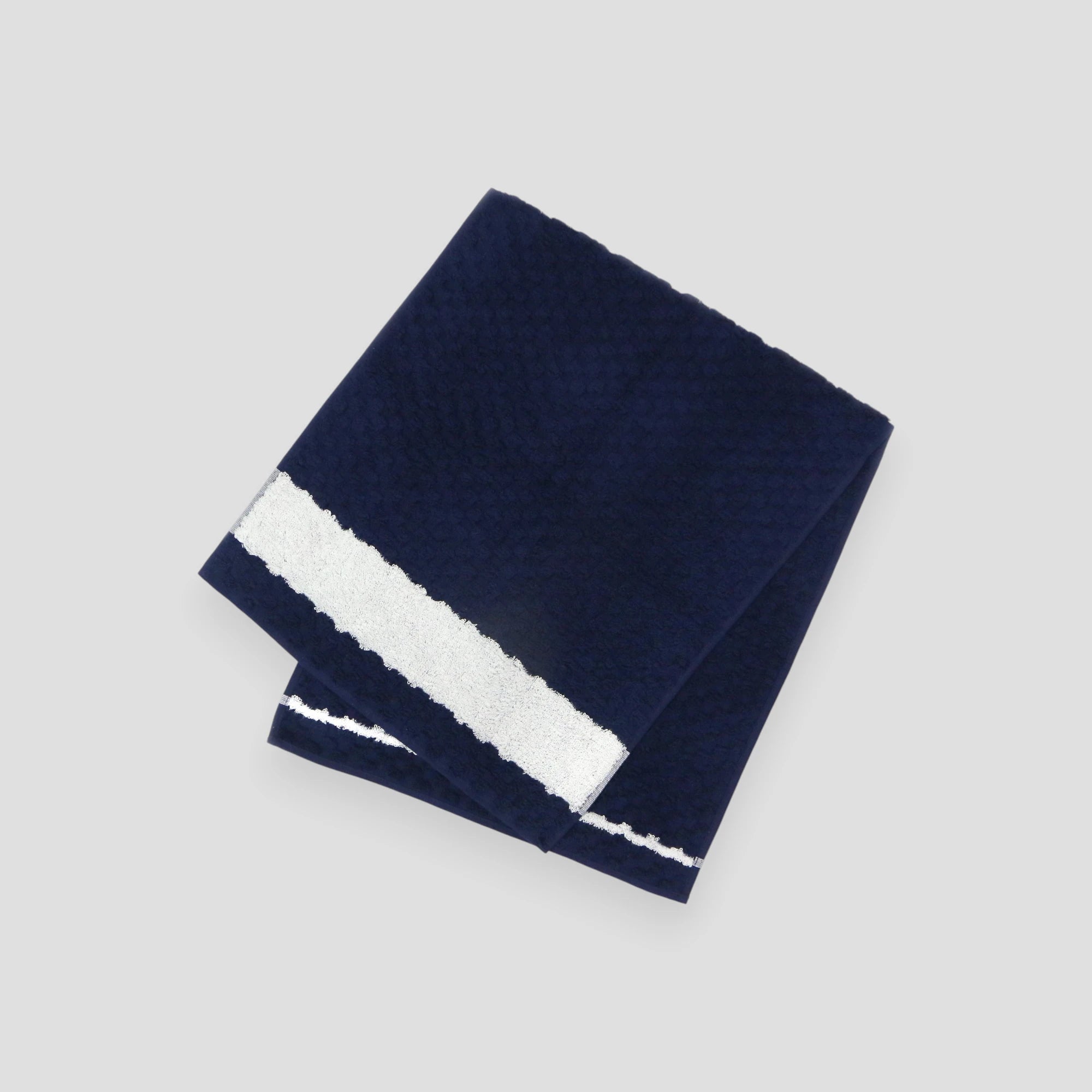 A folded navy with white line jacquard weave towel with a textured design, made of cotton, displayed against a neutral background.