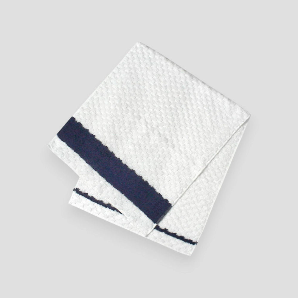 A folded white with navy line jacquard weave towel with a textured design, made of cotton, displayed against a neutral background.