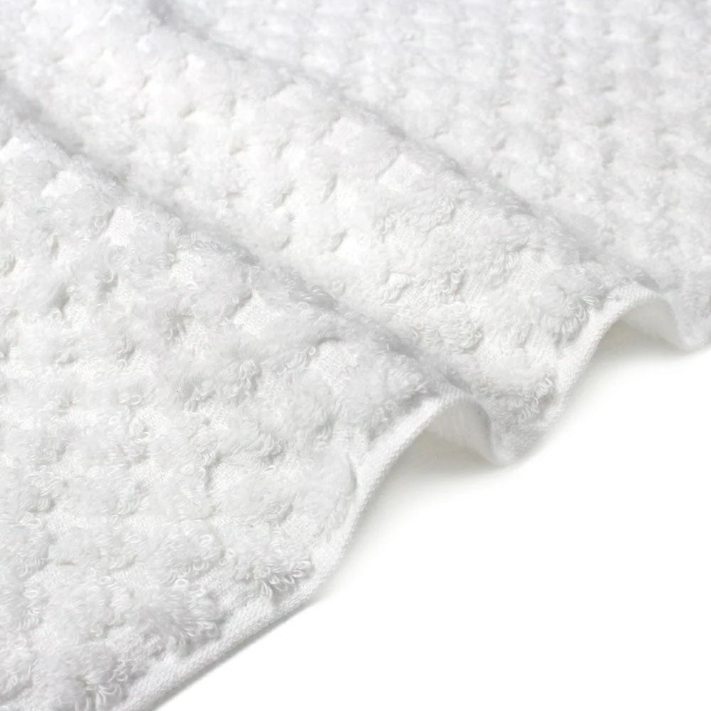 Close-up white jacquard weave Imabari towel corner with a textured design on a light gray background.