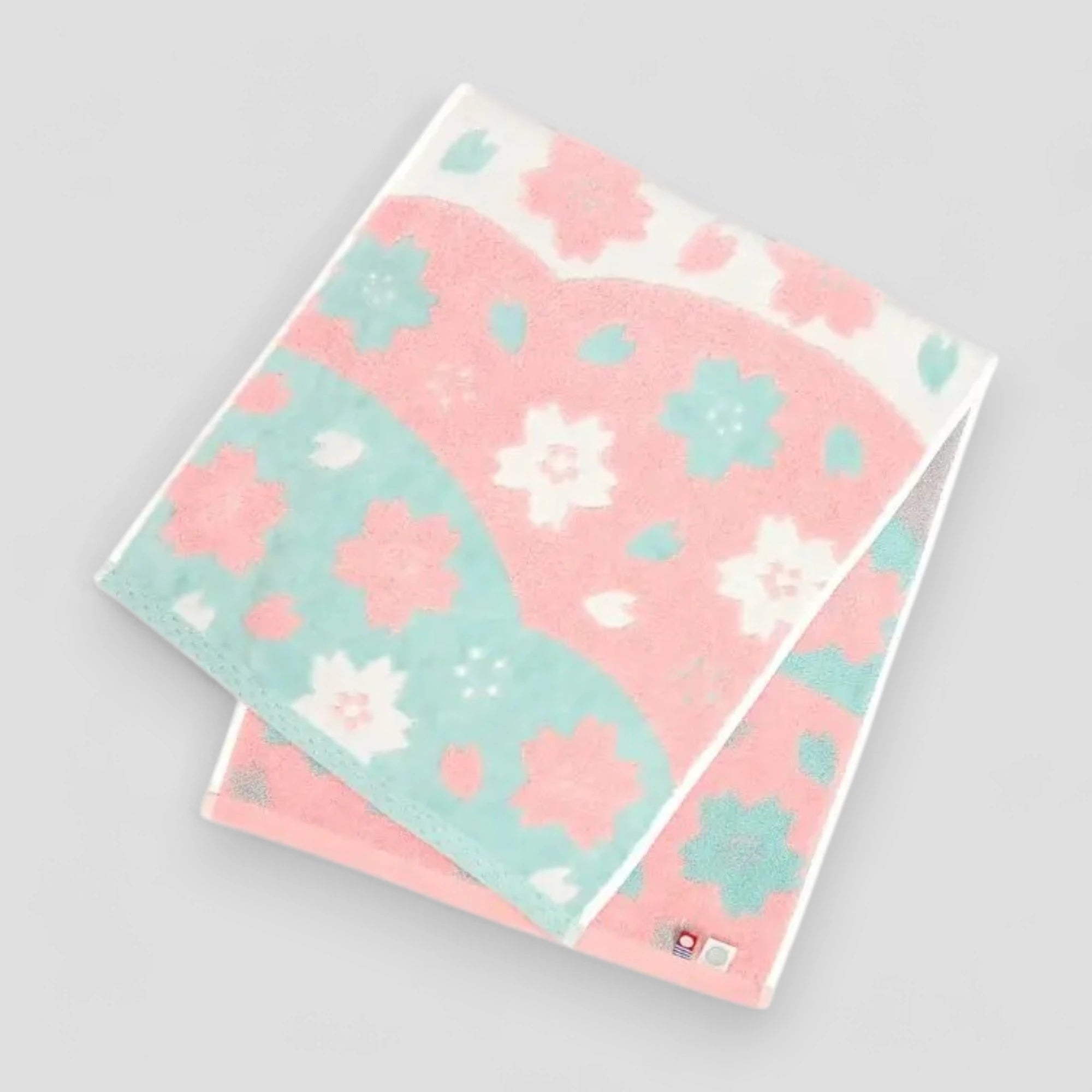 Folded cotton Imabari towel with a floral jacquard pattern in pink, white, and blue colors.